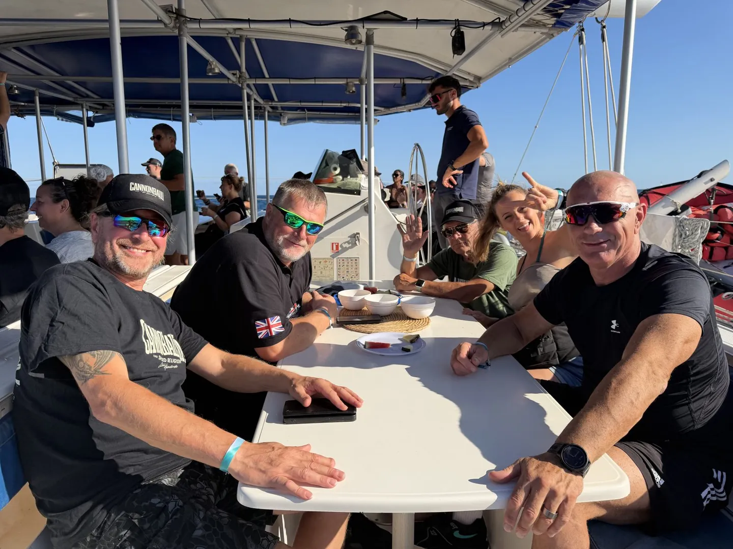 Riders sitting around a table on the deck of a catamaran in the Mediterranean sunshine off Alicante