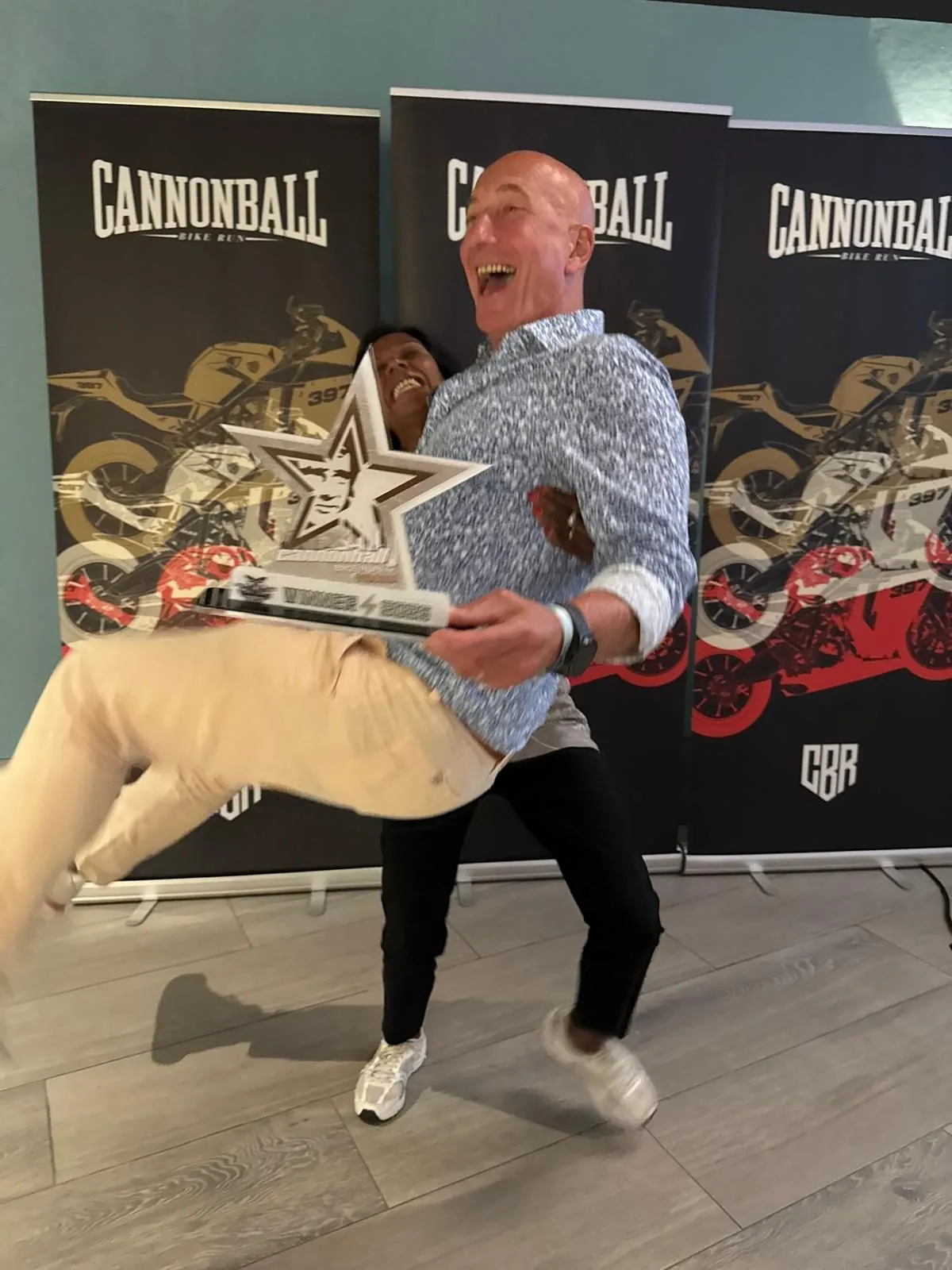 Lars from Norway laughing as he holds his star-shaped Cannonball Legend award in front of event banners