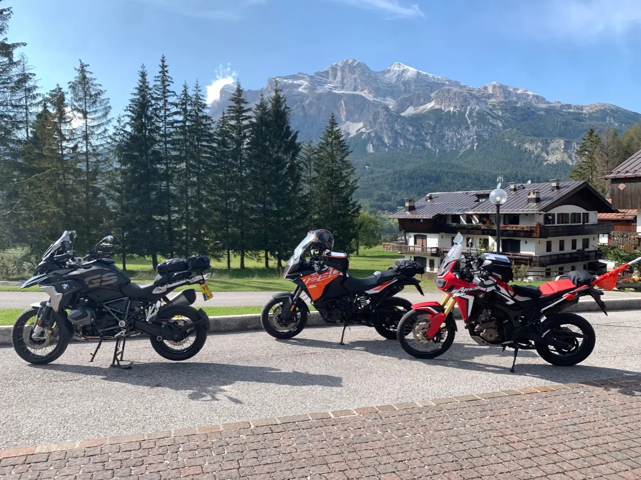 Three adventure motorcycles parked at Cortina d'Ampezzo with the Tofane massif behind