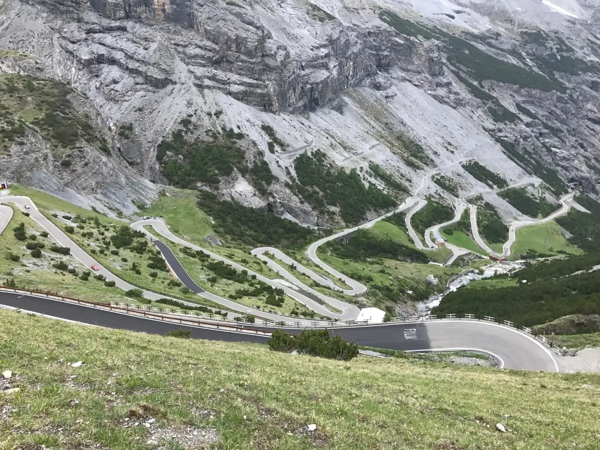 Stacked hairpin bends of the Stelvio Pass climbing the mountainside, photographed from above on the Grand Alpine Traverse